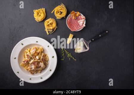 Draufsicht Pasta Fettuccine mit Pilzen, Speck und Parmesan auf dunklem Graphit-Holzhintergrund mit Kopierfläche Stockfoto