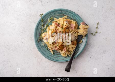 Draufsicht Pasta Fettuccine mit Pilzen, Speck und Parmesan in weißer Platte auf hellem Holzhintergrund mit Kopierfläche Stockfoto