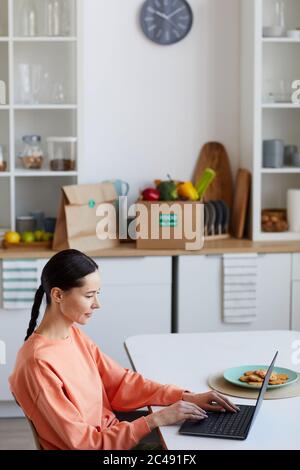 Junge Frau am Tisch sitzen und tippen auf Laptop-Computer in der Küche sie online zu Hause arbeiten Stockfoto
