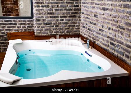 Das Innere des Badezimmers. Ein großes Jacuzzi-Bad steht in der Mitte eines hellen, geräumigen Steinzimmers dekoriert. Modern, Öko, Fenster, Grün. Stockfoto