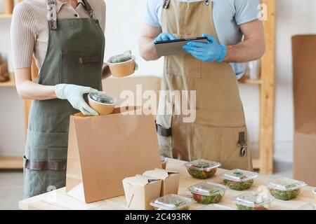Nahaufnahme von zwei Arbeitern in Schutzhandschuhen, die im Lieferservice arbeiten, sie packen Lebensmittel in Papiertüten Stockfoto