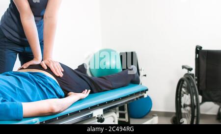 Physiotherapeut, der mit behinderten Menschen im Rollstuhl auf einem Therapietisch trainiert. Stockfoto