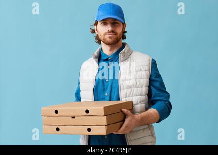 Porträt eines jungen Mannes in Uniform liefern Pizza er Blick auf die Kamera, während vor dem blauen Hintergrund stehen Stockfoto