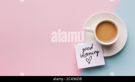 Panoramablick von oben auf eine Tasse Kaffee und ein Beachten Sie Guten Morgen auf einem blauen und rosa Hintergrund Stockfoto