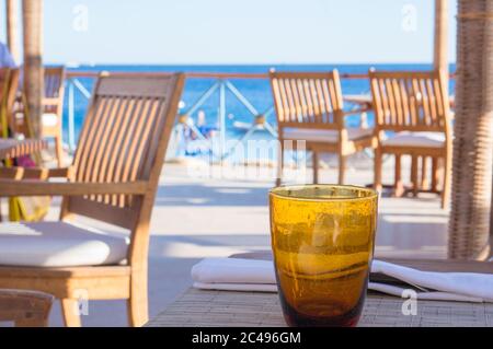 Ein leeres orangefarbenes Glas, das auf dem Tisch im Strandcafé mit Meerblick steht Stockfoto