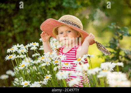 Nettes kleines Mädchen im Sommerkleid und Hut Spaziergänge im Garten unter Gänseblümchen Stockfoto