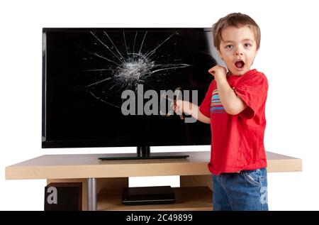 Schockierter kleiner Junge mit einer Schleuder, der vor einem Fernseher mit kaputter Leinwand stand. Hausversicherungskonzept. Studio-Aufnahme isoliert auf weißem Hintergrund. Stockfoto