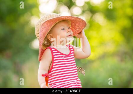 Nettes kleines Mädchen in einem roten Kleid und Hut geht im Sommer barfuß auf dem grünen Gras, Platz für Text Stockfoto