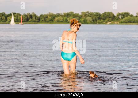 Reife kaukasische Frau spielt Ball im Wasser mit Hund der Rasse Dachshund. Sommerthema mit Haustieren schwimmen im Fluss. Heißes Wetter im Sommer. Kühlen Stockfoto