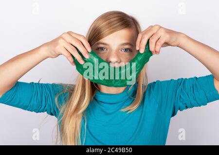 Nettes Mädchen, das ein Lächeln mit einem grünen Schleim Spielzeug vor ihrem Gesicht macht Stockfoto