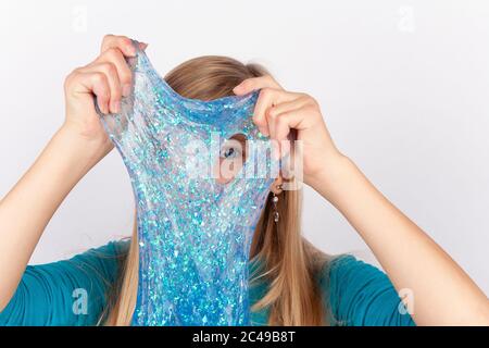 Lustiges Mädchen hält einen blauen Glitzer Schleim vor ihrem Gesicht und schaut durch sein Loch. Stockfoto