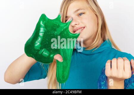 Mädchen hält einen transparenten blauen Glitzer und einen grünen Schleim an den Händen. Konzentriert sich auf die Slimes Stockfoto