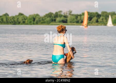 Kaukasische ältere Frau, die Spaß am Sommerwochenende mit ihrem Hund Rasse Dackel im Wasser. Ältere Frau, die Outdoor-Aktivitäten im Fluss genießt Stockfoto