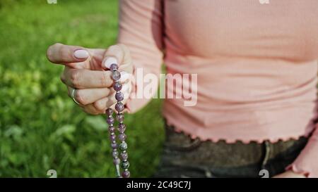 Frau beleuchtet Hand Nahaufnahme zählt Rosenkranz - Malas Stränge von Edelsteinen Perlen für Zählung während Mantra Meditationen verwendet. Mädchen sitzt auf Sommer Natur Stockfoto