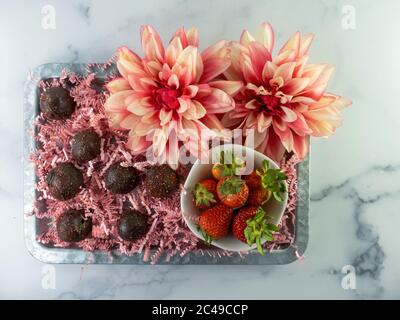 Draufsicht auf Schokoladenkugeln mit frischen Erdbeeren in einem Tablett mit Blumen auf einem weißen Marmortisch Stockfoto