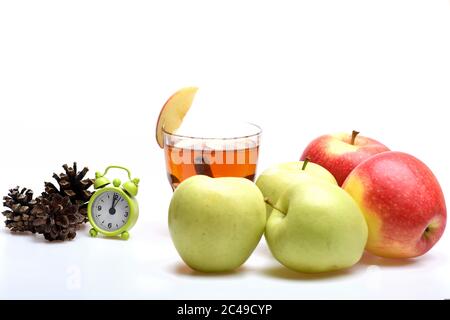 Zusammensetzung von Äpfeln und rustikalem Gefolge. Obstset neben einem Glas Tee mit Zimt, Tannenzapfen und winzigem Wecker. Eco Style und Gemütlichkeit Konzept. Äpfel und Tee isoliert auf weißem Hintergrund Stockfoto