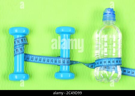 Zwei Kunststoff-Kurzhanteln und Flasche. Satz Handgewichte auf hellem Hintergrund. Zwei blaue Fitness-Hanteln, Zentimeter und eine Flasche Wasser auf grünem Hintergrund. Gesundes Lifestyle- und Trainingskonzept. Stockfoto