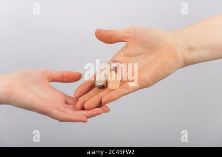 Hand, die einer anderen Hand ein Hörgerät gibt Stockfoto