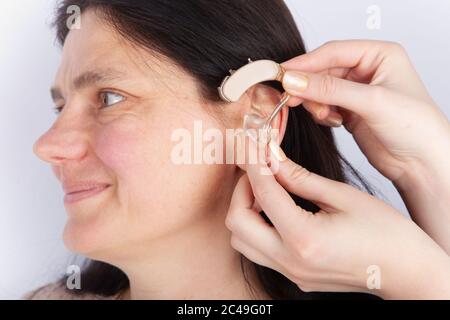 Nahaufnahme des Ohres einer Frau und der Hand eines Audiologen mit Hörgerät Stockfoto