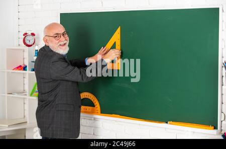 Tutor Mann in Brille zeichnen mit Dreieck auf Tafel. Zurück zur Schule. Welchen Winkel Sie suchen. Geometrische Formen. High School moderne Bildung. Senior man Lehrer verwenden Triagle beim Zeichnen. Stockfoto