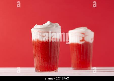 Erdbeer Smoothie Shakes im Glas mit Schlagsahne auf rotem Hintergrund.Sommer erfrischenden Getränk Mocktail Stockfoto