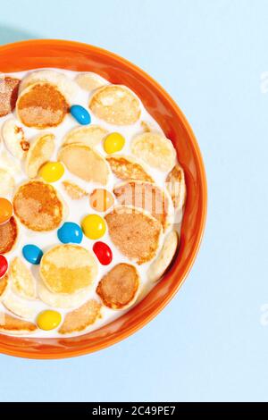 Orange Schüssel mit winzigen Pfannkuchen Cerealien Brei mit Milch auf einem blauen Hintergrund Draufsicht close-up.trendy leckeres Frühstück Essen Stockfoto