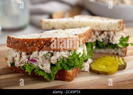 Thunfisch-Salat und Salat-Sandwich in zwei Hälften auf Mehrkernbrot mit geschnittenen Gurken auf einem Holzbrett geschnitten Stockfoto