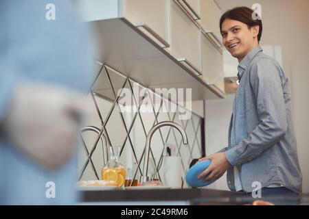 Positive Mann waschen das Geschirr und schauen begeistert Stockfoto