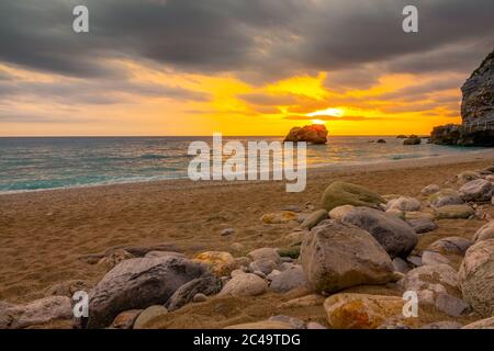 Grober Sandstrand mit Steinen. Farbenprächtiger Sonnenuntergang über dem ruhigen Meer Stockfoto