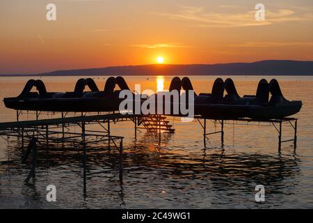 Schöner Sonnenuntergang über dem Plattensee mit Tretbooten im Vordergrund. Stockfoto