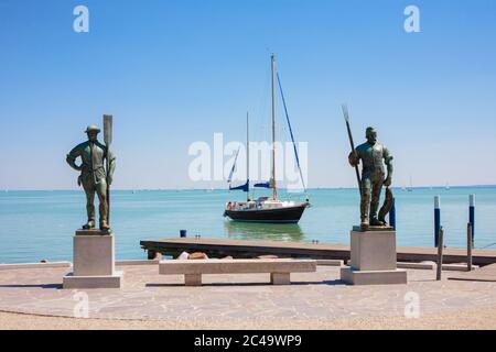 BALATONFÜRED, UNGARN - 03. AUGUST 2013: Fischer- und Rudermännchen Statuen am Strand von Balatonfüred mit einem Segelboot im Hintergrund am Balatsee Stockfoto