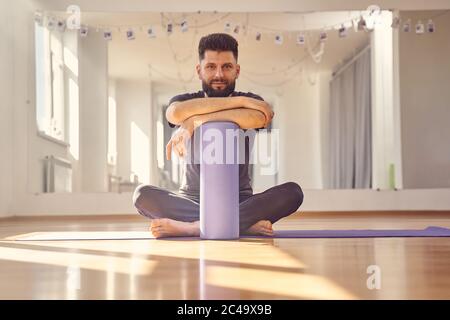 Bärtiger Mann mit Schaumstoffrolle sitzt auf dem Boden im Yoga-Studio Stockfoto