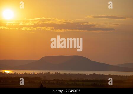 Sonnenuntergang mit Lichtreflexe über dem Plattensee und Badacsony Berg in Ungarn Stockfoto