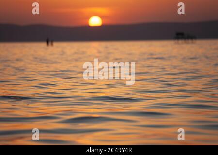 Verschwommener Sonnenuntergang über dem Plattensee in Ungarn. Fokussiert auf Wellen im Vordergrund Stockfoto