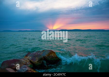 Schöner Sonnenuntergang mit Sonnenstrahl über dem stürmischen Plattensee in Ungarn Stockfoto