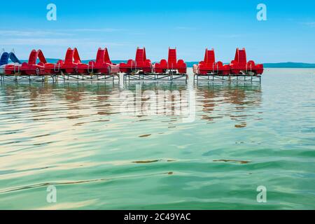 Reisehintergrund von roten Tretbooten auf einem Pier mit großer Wasseroberfläche in der Front am Plattensee in Ungarn Stockfoto