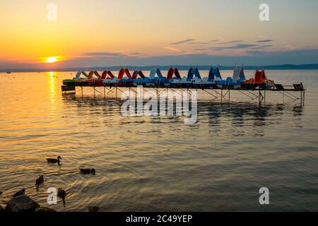 Reise Hintergrund der bunten Tretboote auf einem Pier mit Enten bei Sonnenuntergang am Plattensee in Ungarn Stockfoto