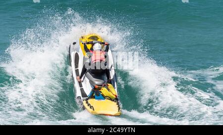 Spektakuläre Action als RNLI Rettungsschwimmer fährt einen Jetski über eine Welle bei Fistral in Newquay in Cornwall. Stockfoto