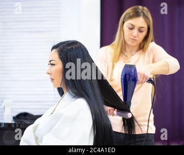 Junge schöne Frau mit schwarzen Haaren beim Friseur. Friseur trocknet Haar für Kunden Stockfoto