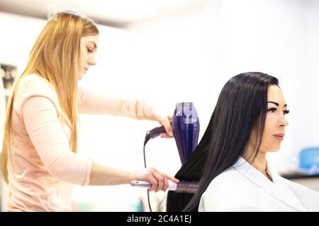 Schöne Frau mit schwarzen Haaren beim Friseur. Friseur trocknet Haar für Kunden Stockfoto