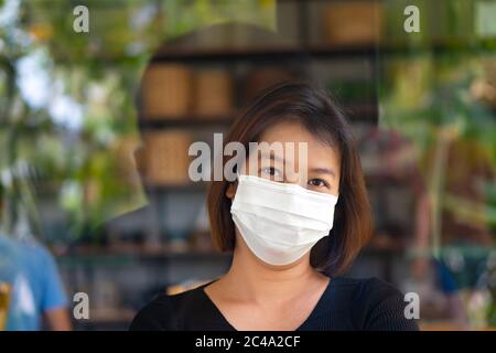 Asiatische Frau trägt Schutzmaske auf ihrem Gesicht, während sie im Café während Virus COVID-19 Pandemie. Stockfoto