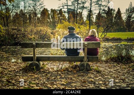 Ein altes Paar sitzt in einem Park und genießt gemeinsam die Sonne. Auf dem Foto geht es darum, zusammen zu bleiben und die Liebe ein Leben lang zu bewahren. Stockfoto