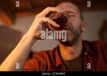Reifer Mann, der zu Hause starken Alkohol aus dem Glas trinkt Stockfoto