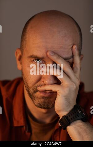 Nahaufnahme eines baldigen reifen Mannes, der sein Gesicht mit der Hand bedeckt und die Kamera anschaut Stockfoto