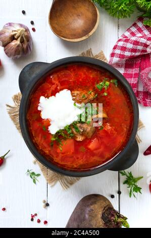 Traditioneller ukrainischer Borsch mit jungem Gemüse und Fleisch in einem schwarzen Tontopf auf weißem Holzgrund. Draufsicht. Stockfoto