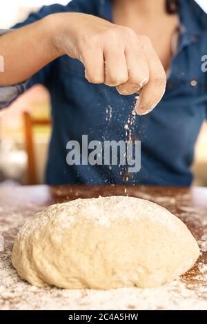 Hände einer Frau, die Mehl auf rohen Teig gießt Stockfoto