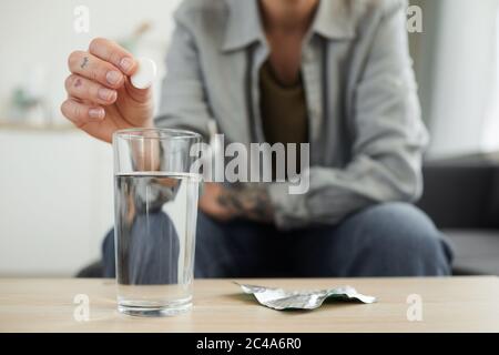 Nahaufnahme einer jungen Frau, die auf dem Sofa vor dem Tisch sitzt und die Pille in das Glas Wasser wirft Stockfoto