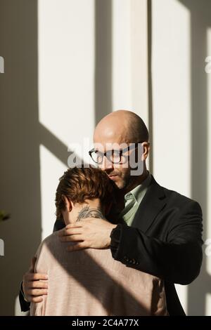 Reifer Mann in Anzug tröstend und umarmt die Frau, während sie im Büro stehen Stockfoto