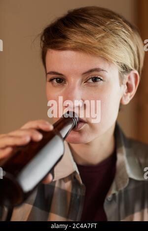 Porträt einer jungen Frau mit kurzen Haaren, die Bier aus der Flasche trinkt und die Kamera anschaut Stockfoto