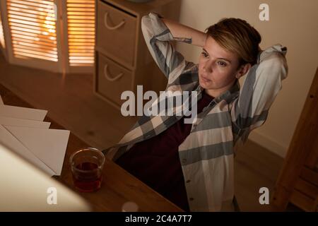 Junge Frau am Tisch mit Dokumenten sitzen sie müde nach der Arbeit und entspannen mit Alkohol Getränke Stockfoto